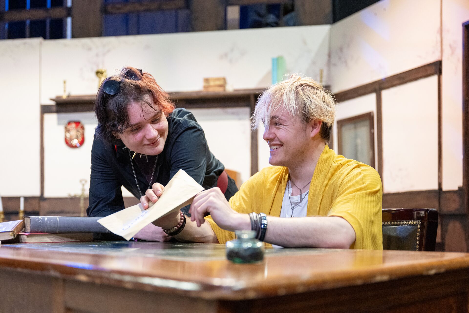 Two actors sat at a desk on stage