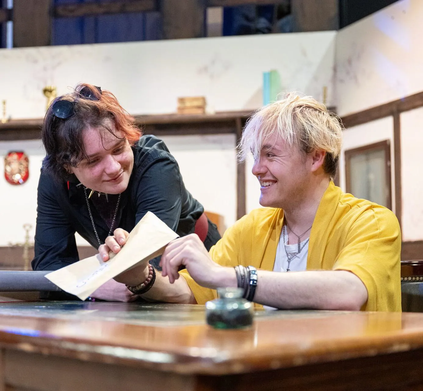 Two actors sat at a desk on stage