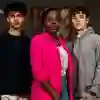 Three students stood in front of hung paintings at an art gallery
