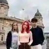 Three students dressed casually looking into the camera while standing in front of a large historical building