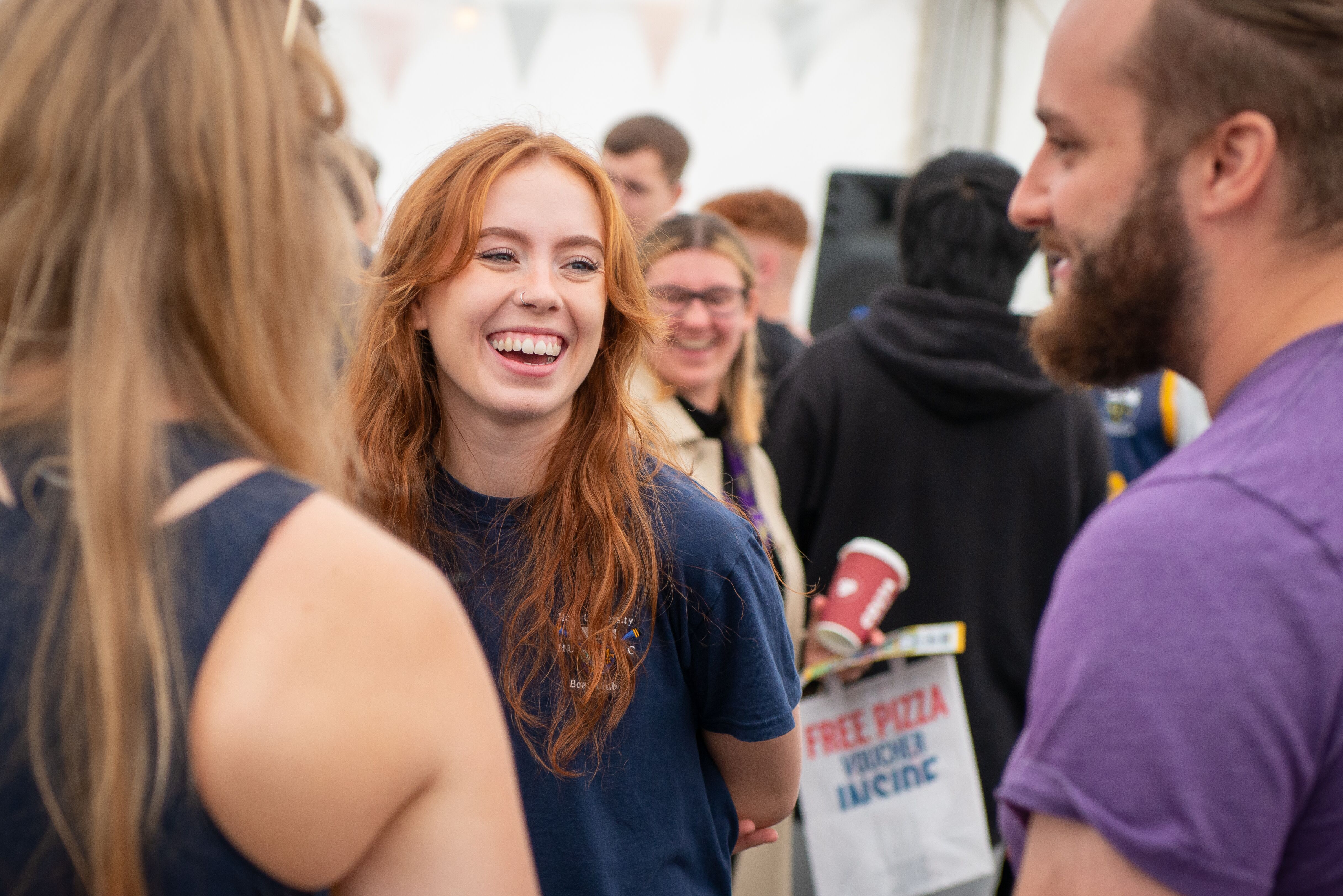 A female student smiles and laughs with friends at the Freshers Fair