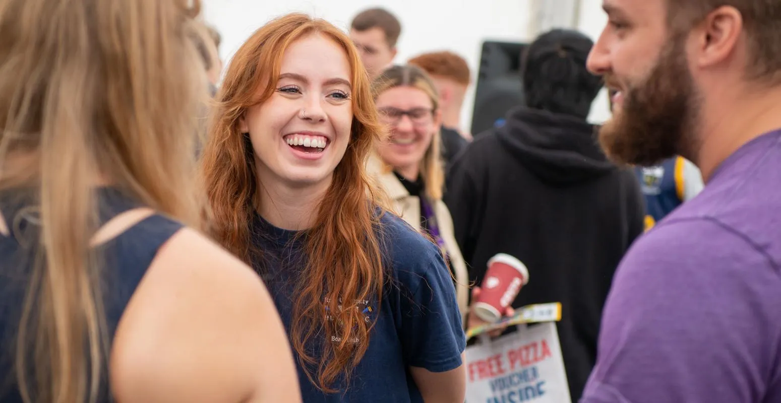 A female student smiles and laughs with friends at the Freshers Fair