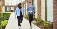 Two students chat while walking outside our modern Westfield Court accommodation blocks.