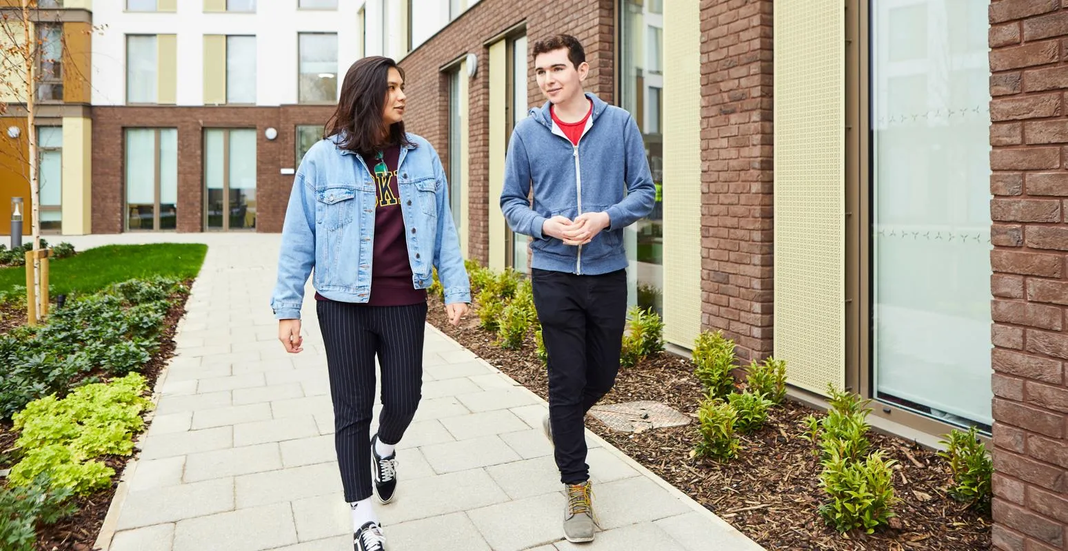 Two students chat while walking outside our modern Westfield Court accommodation blocks.