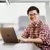 Student in library with laptop, smiling at the camera.