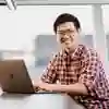 Student in library with laptop, smiling at the camera.