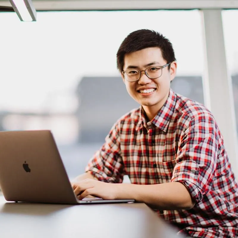 Student in library with laptop, smiling at the camera.