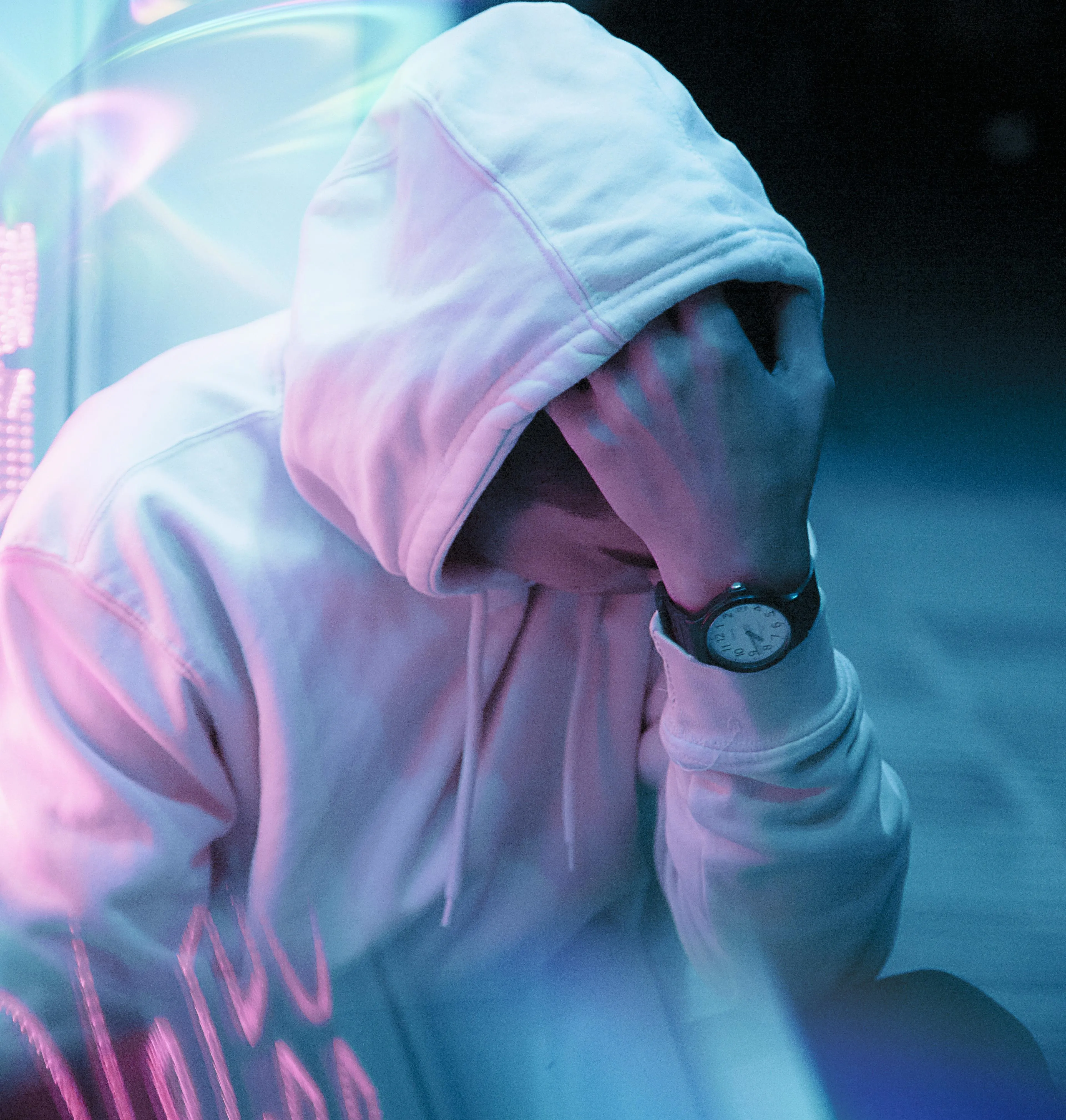 young male wearing white hooded top sitting hand up to his head covering face
