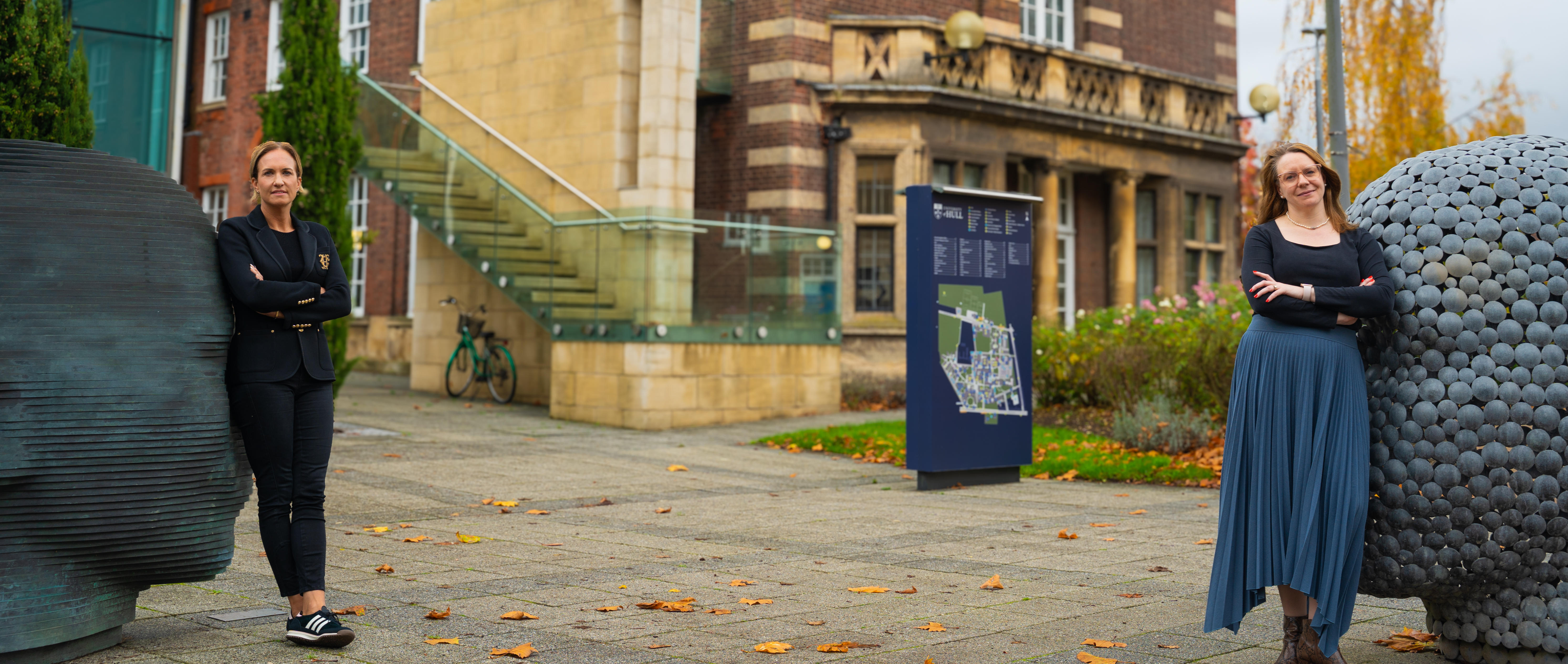 two women leaning against head sculptures at entrance to business school