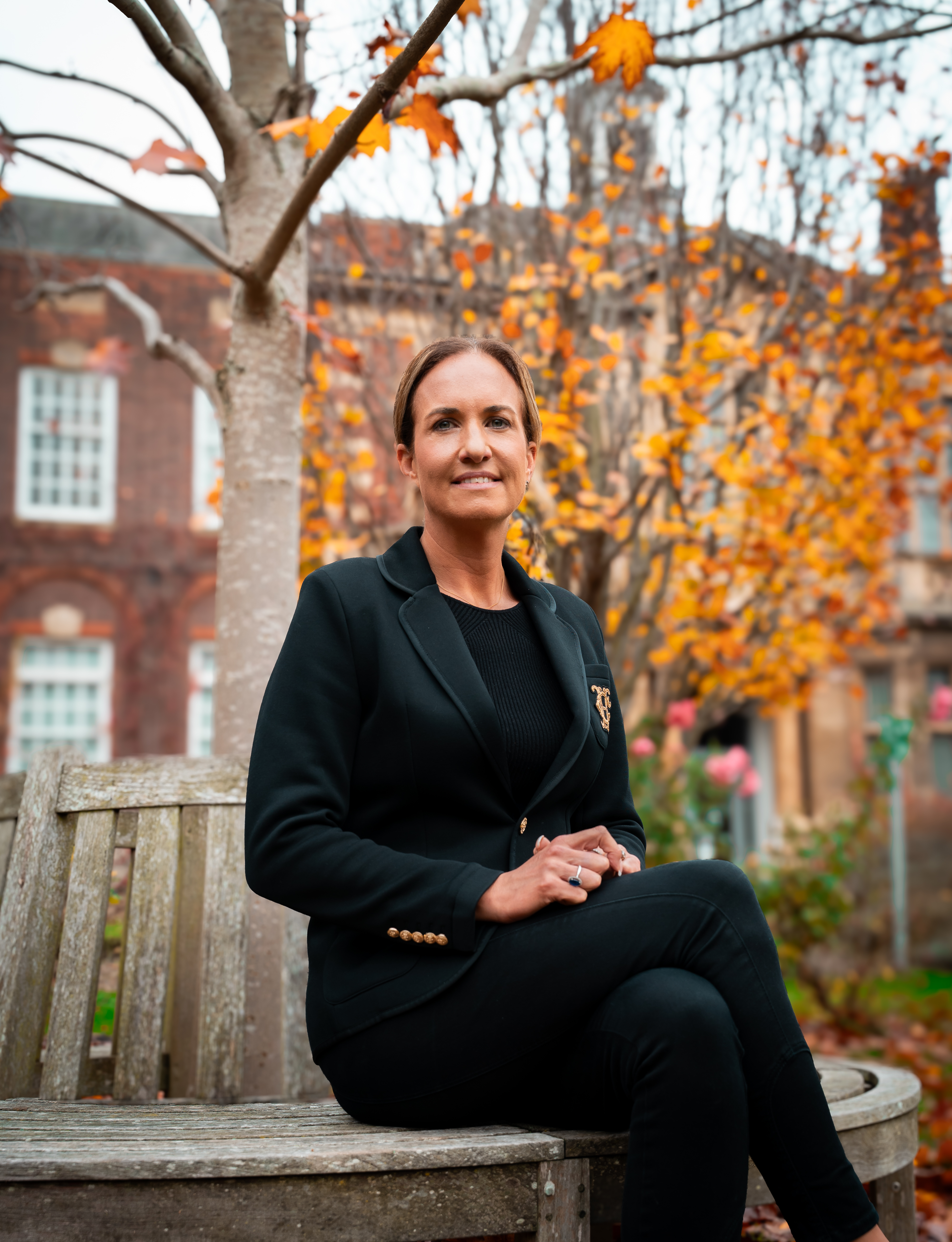 woman sitting on a bench with trees and building behind