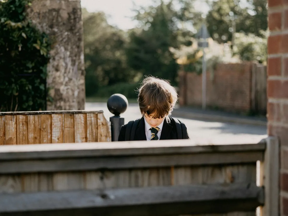 head and shoulders of boy in school uniform behind a gate looking down