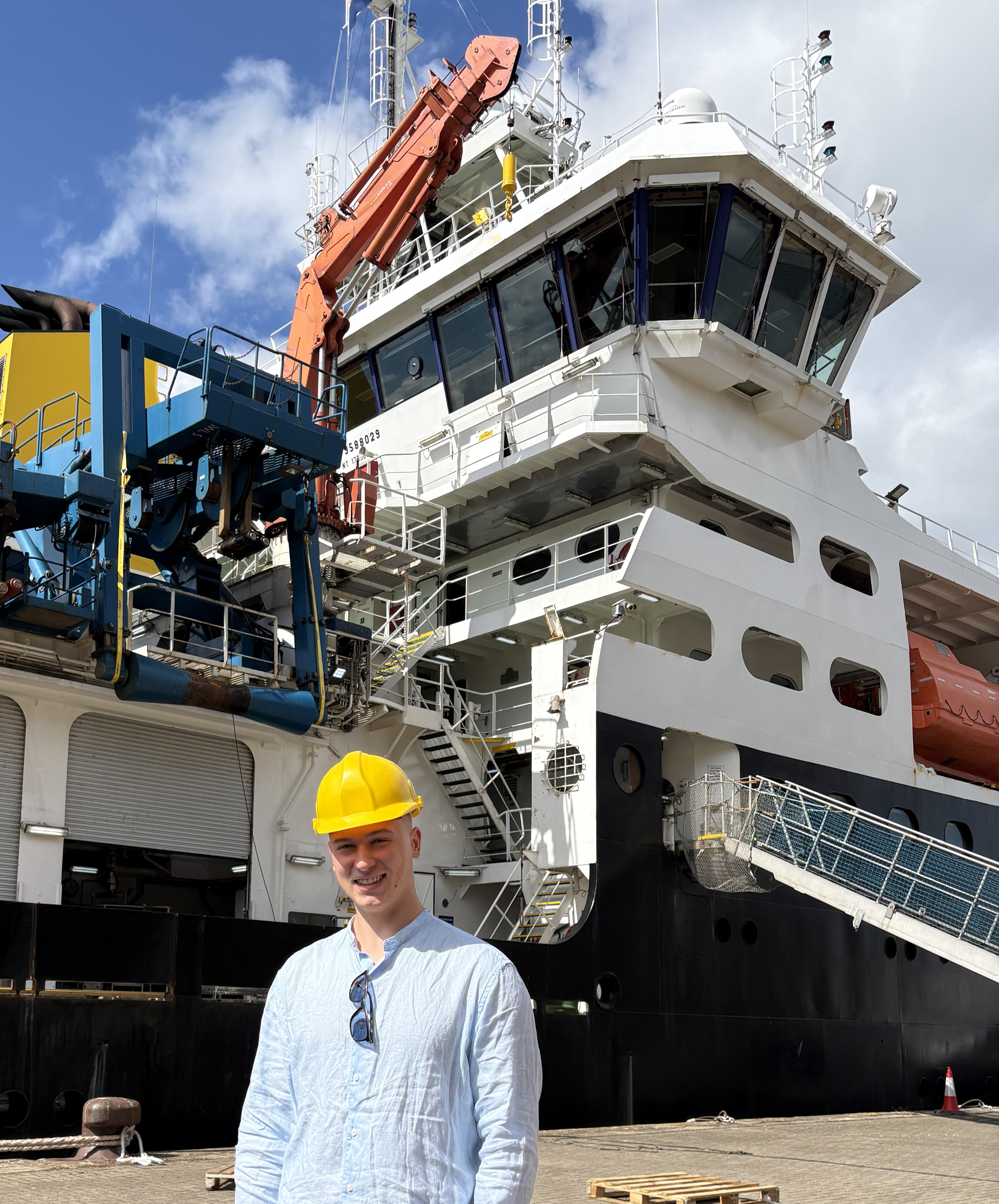 Ben in hard hat on quayside standing in front of RSS Discovery 