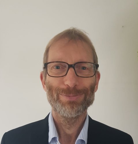 head and shoulders shot of bearded, bespectacled man looking straight at camera and smiling