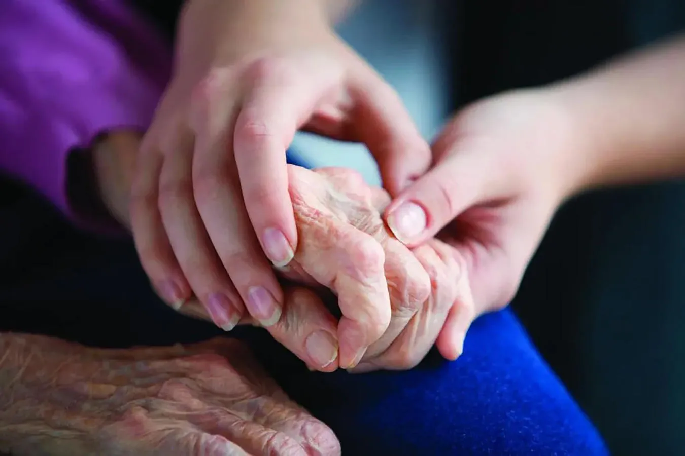An elderly person is supported by a younger person, with hands clasped