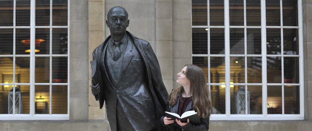 Person standing with a book looking at statue of Philip Larkin