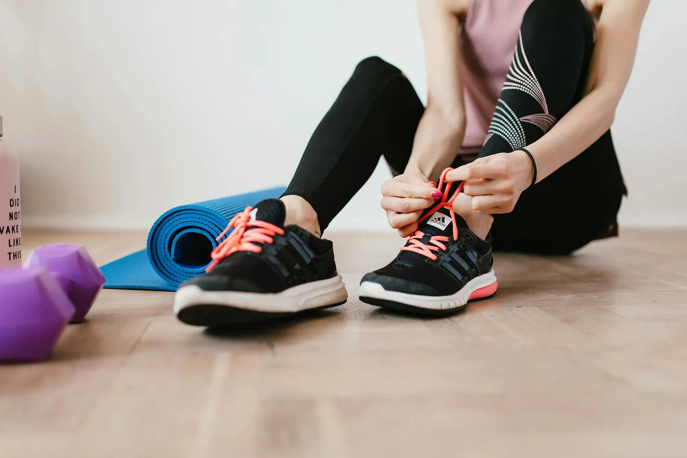 A woman in exercise clothing is tying her trainer shoelaces