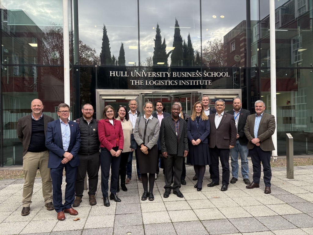group on paved area in front of glass entrance to Logistics Institute facing camera