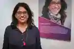 Indhu Rubasingham standing in front of a panel celebrating her achievement