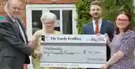 Four people hold a presentation sized cheque for £50,000 from the Lords Feoffes to IntoUniversity
