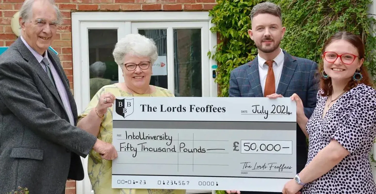 Four people hold a presentation sized cheque for £50,000 from the Lords Feoffes to IntoUniversity