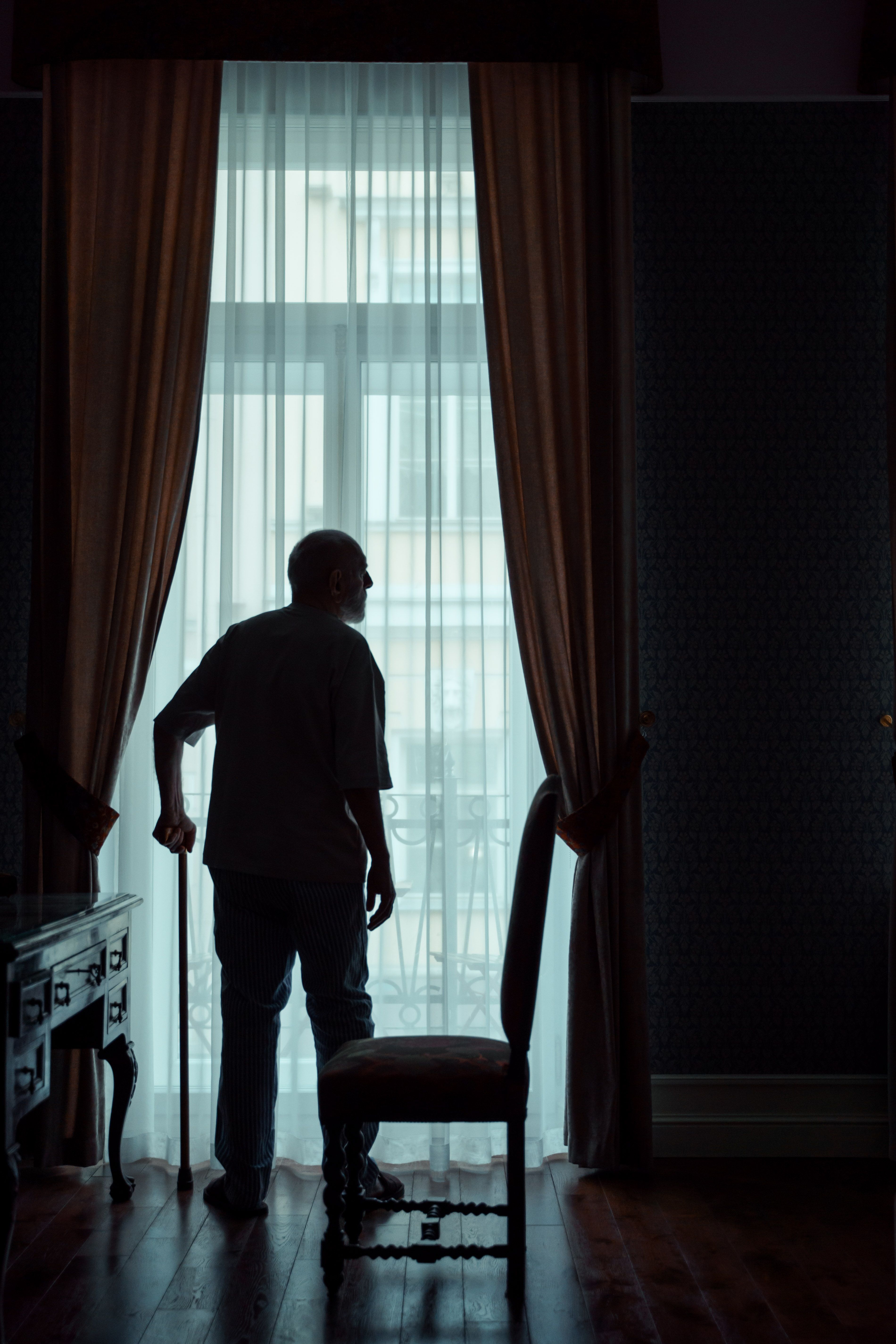 older man with walking cane standing at window 