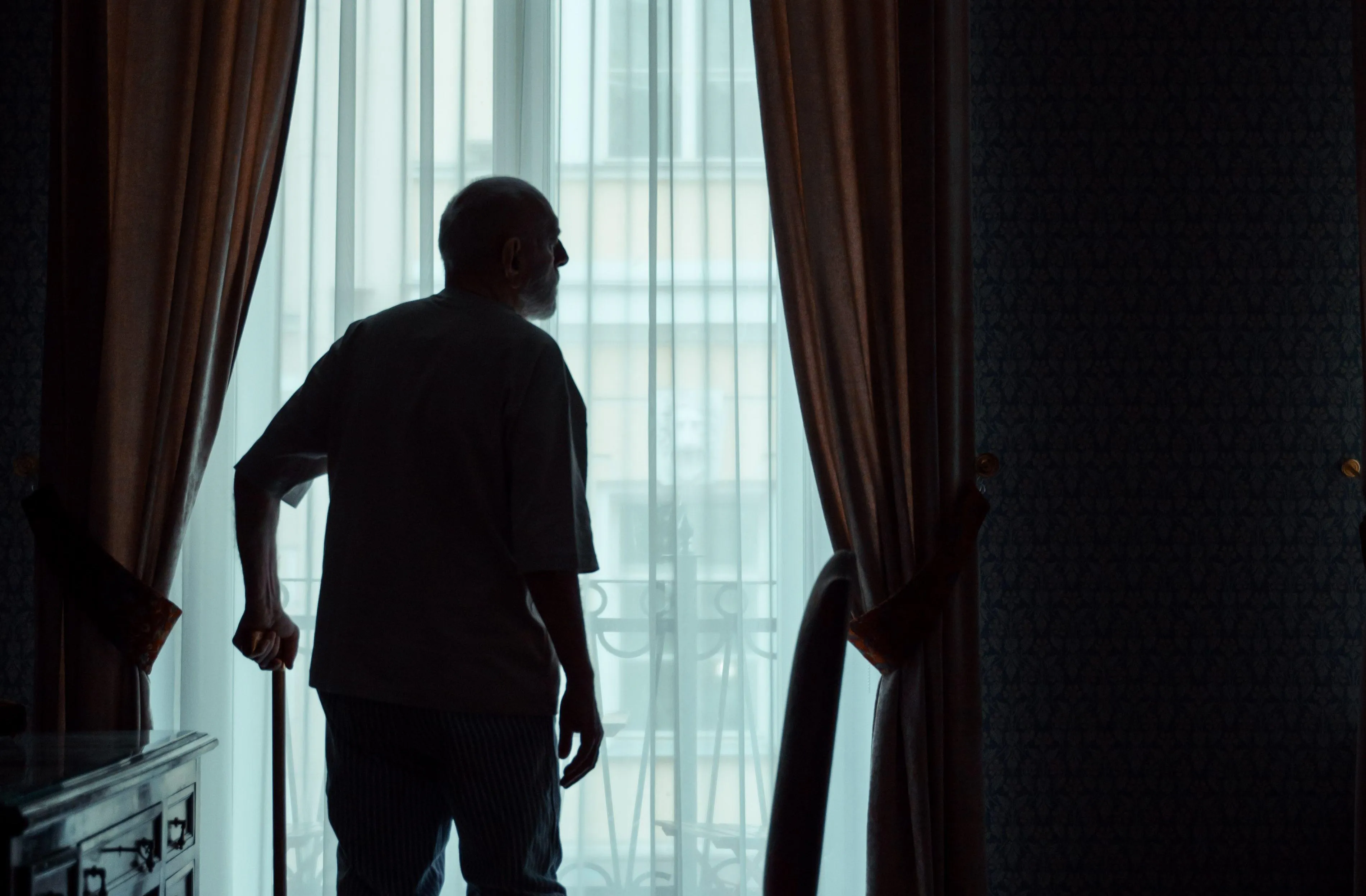 older man with walking cane standing at window