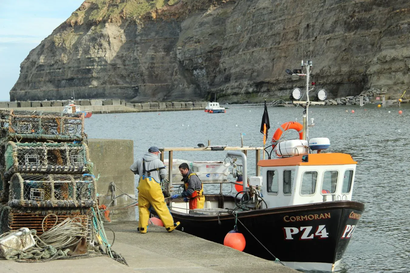A fishing boat and two crew moored in Whitby harbour