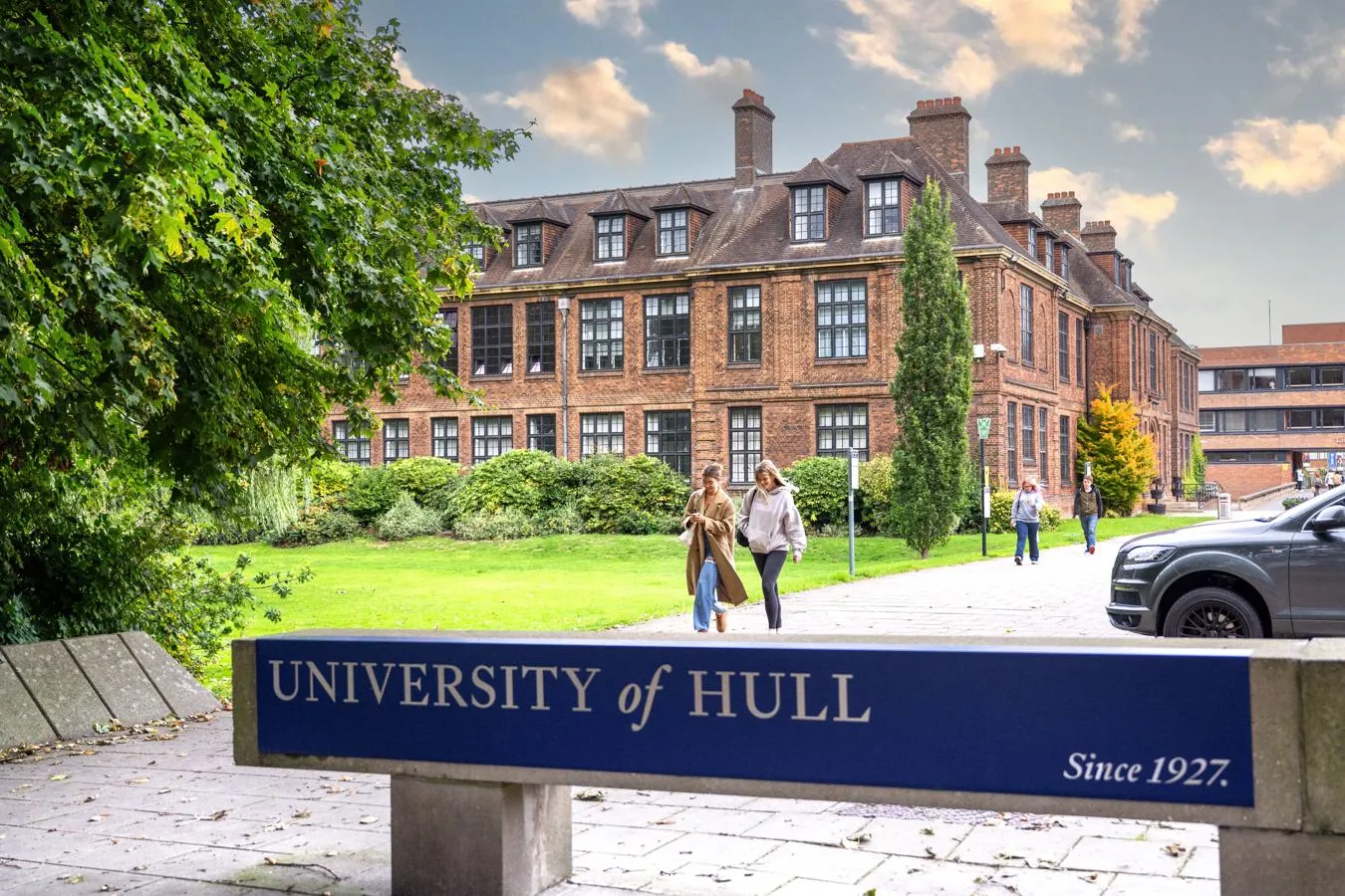 The University of Hull sign with a building in the background and students walking