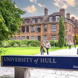 The University of Hull sign with the campus in the background and students walking