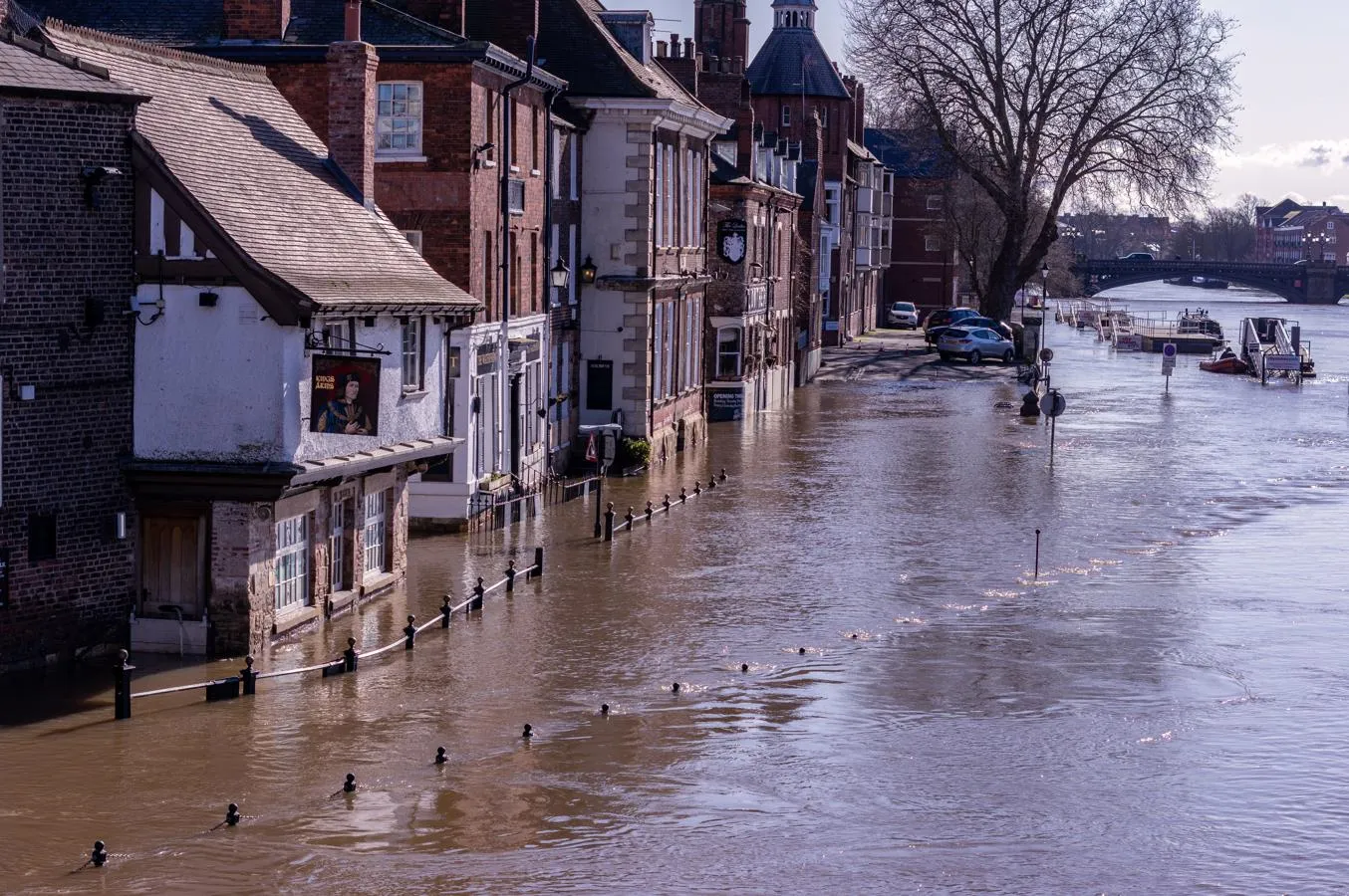 a riverside street with buildings and cars affected by flooding following the river bursting its banks