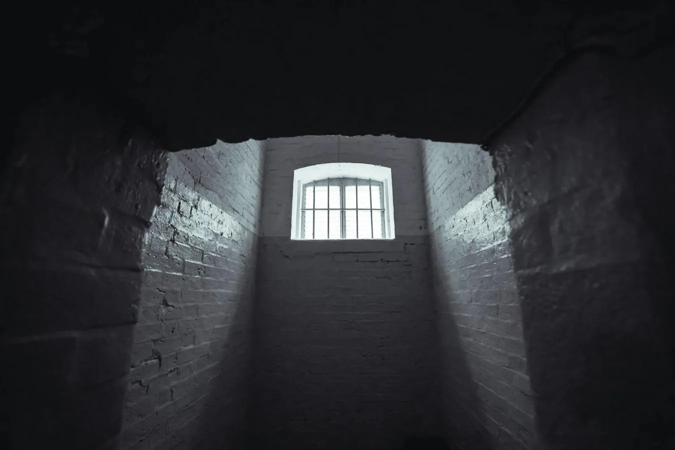 A barred window illuminates a bare prison cell