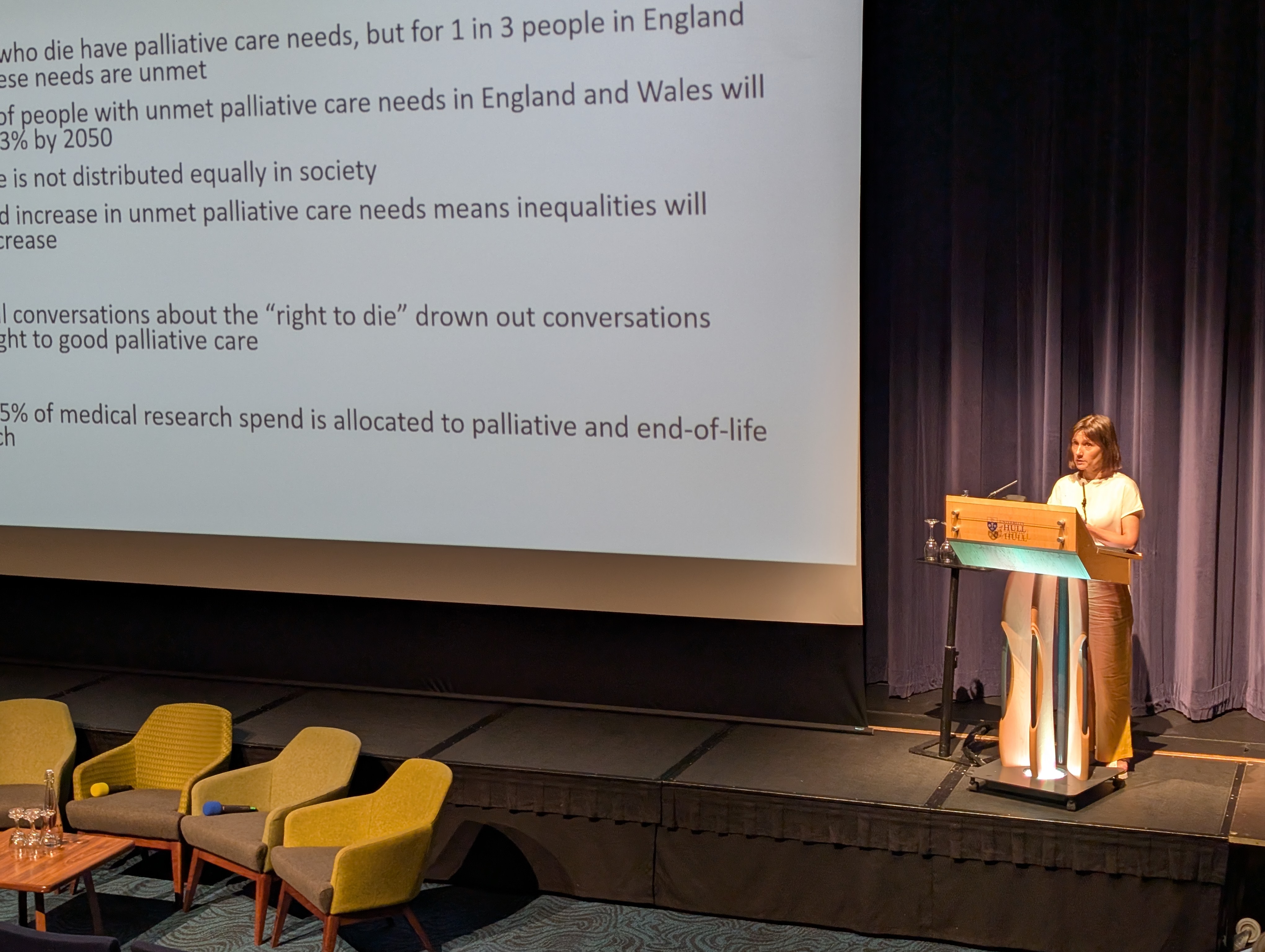 woman at lectern presenting on stage beside slide