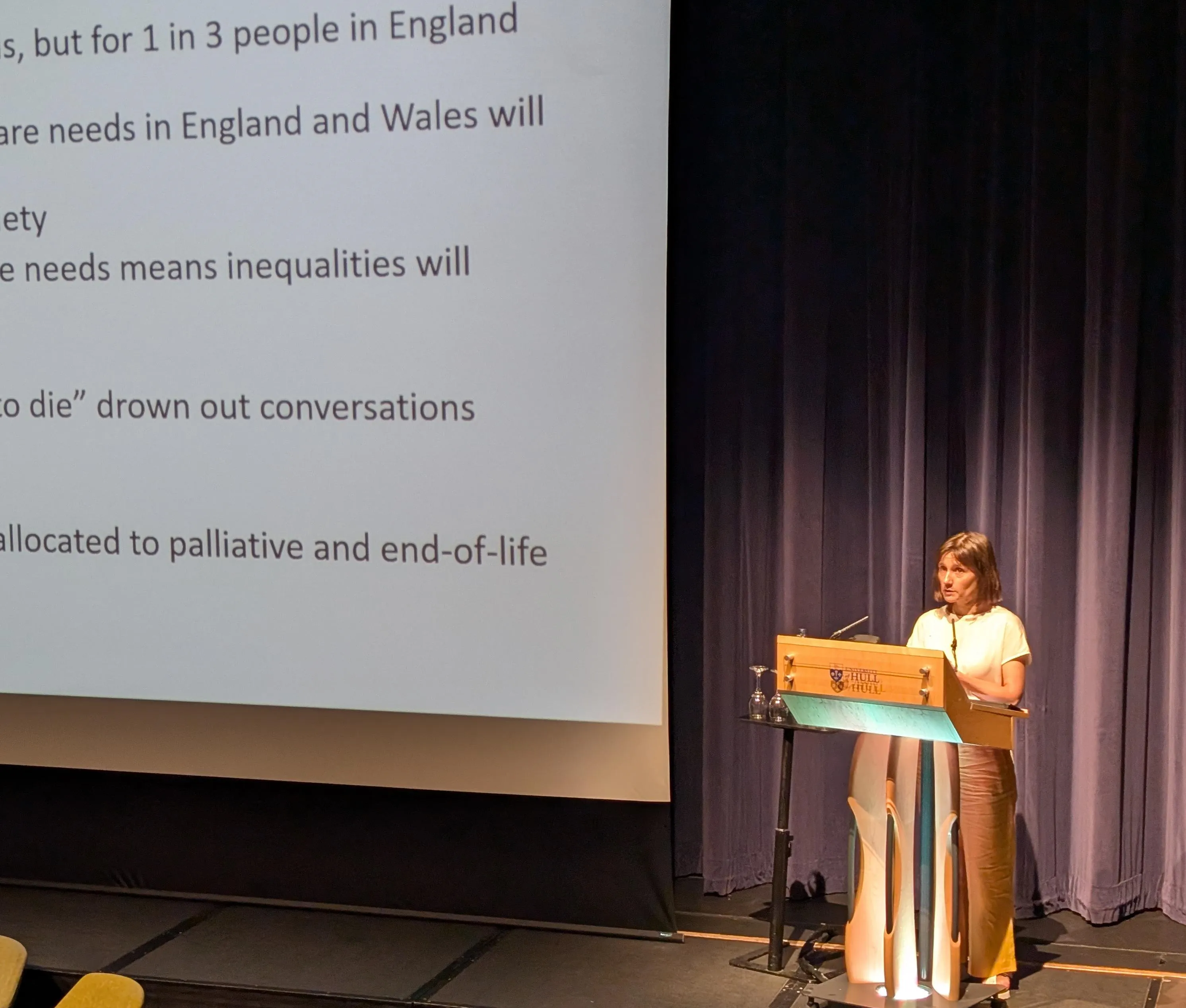 woman at lectern presenting on stage beside slide