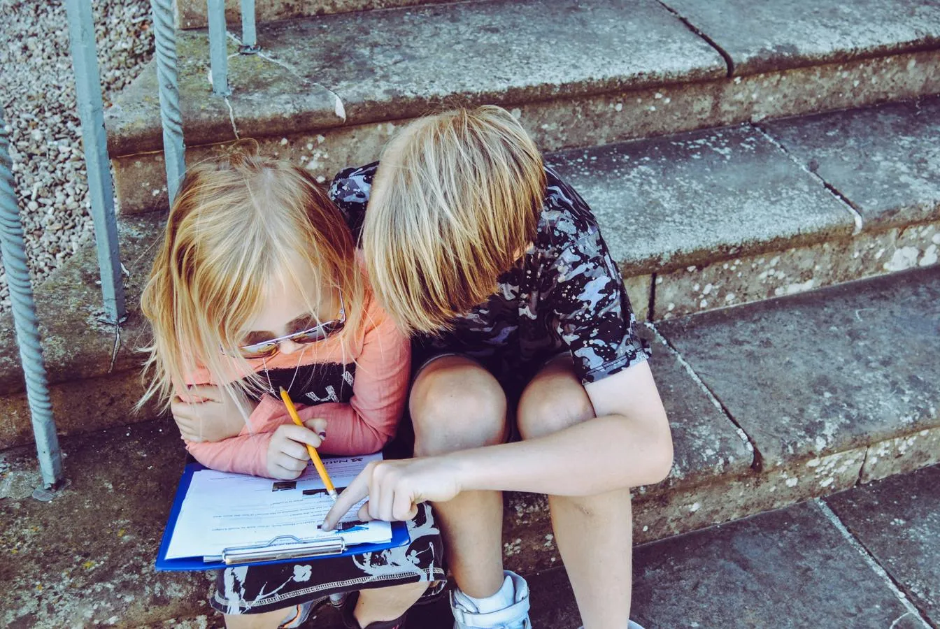 two children sitting on steps completing a paper questionnaire