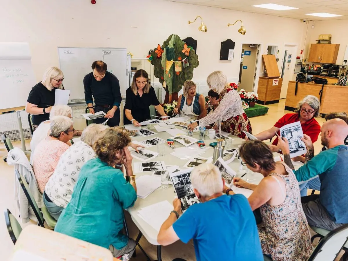 Community group working around a large table handling and viewing a variety of images