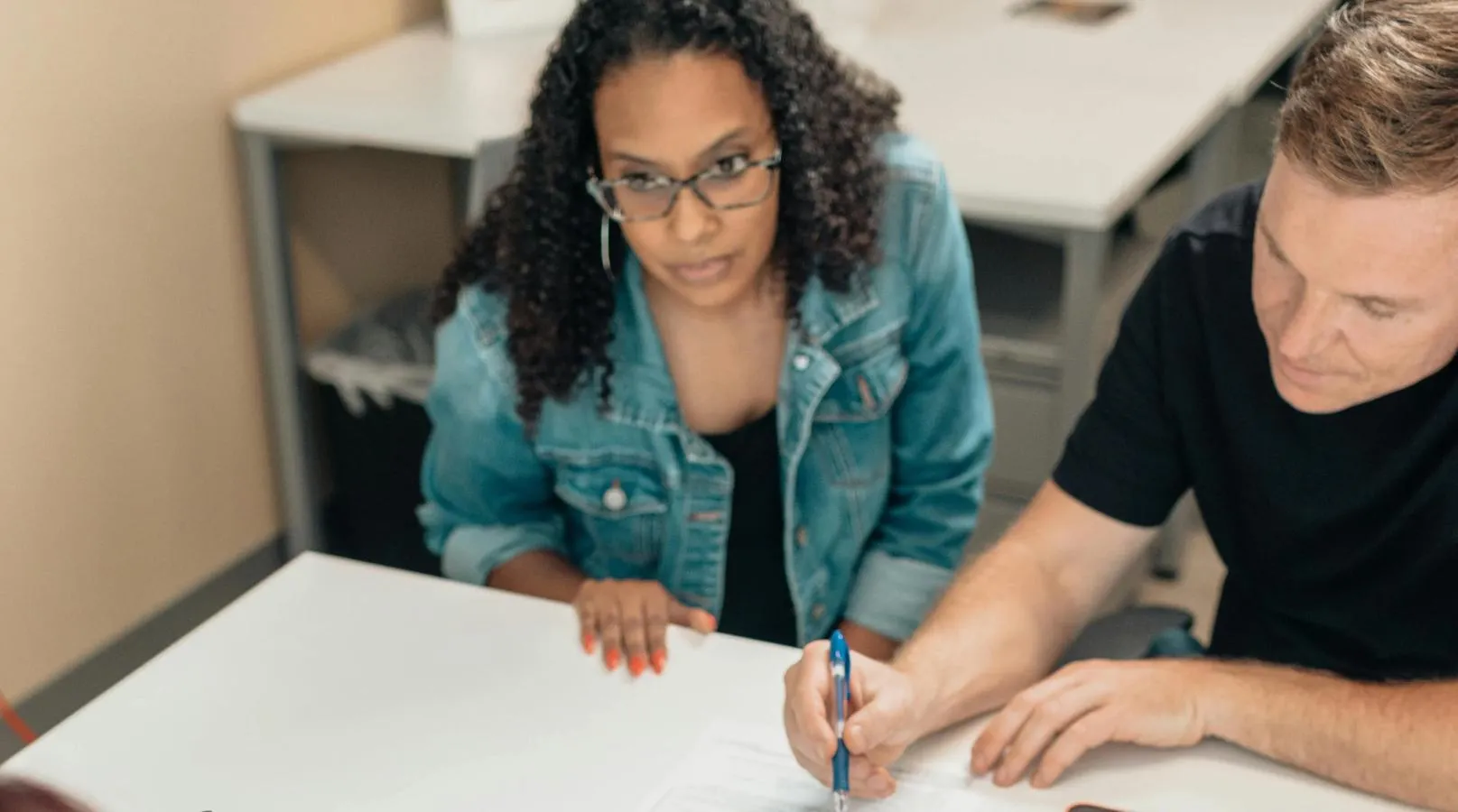 a woman and man sitting behind a desk, he is making notes on a document in front of them