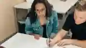 a woman and man sitting behind a desk, he is making notes on a document in front of them