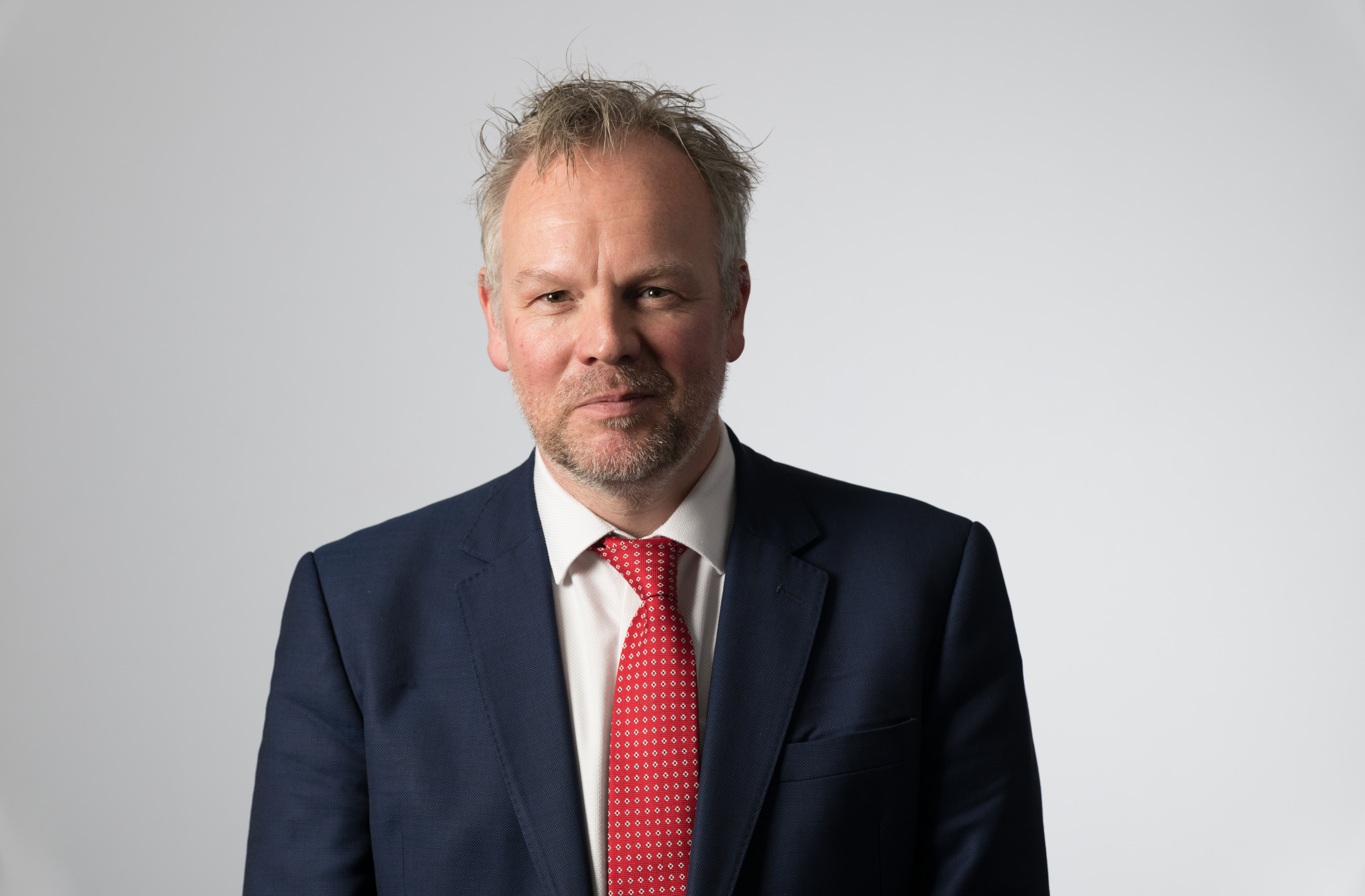 Portrait, head aand shoulders shot of man in dark suit and red tie facing camera