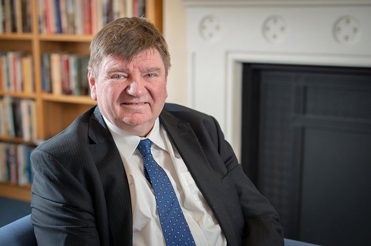 Professor Burnard sat on a chair in front of a bookcase. 
