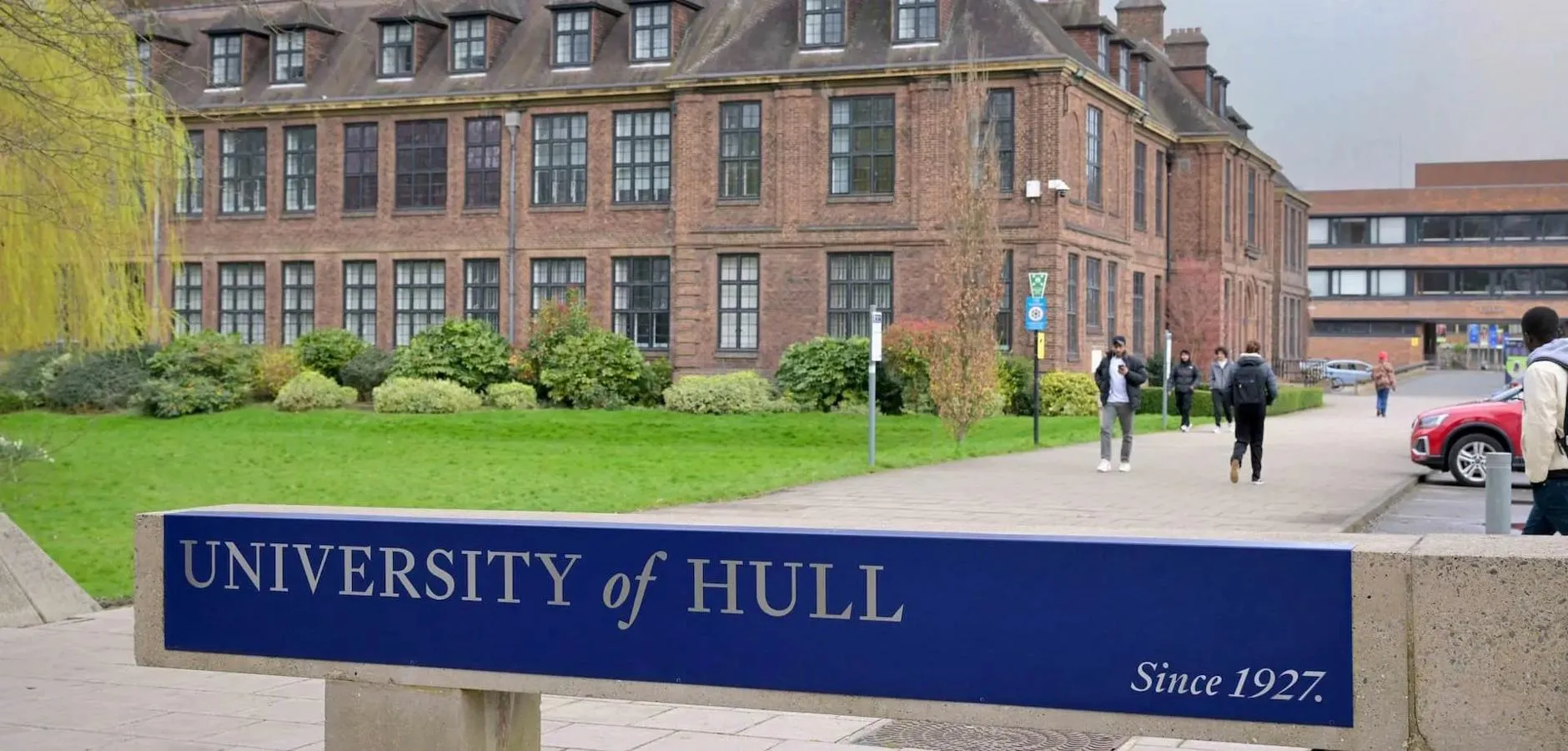 University of Hull sign at front of campus with students walking
