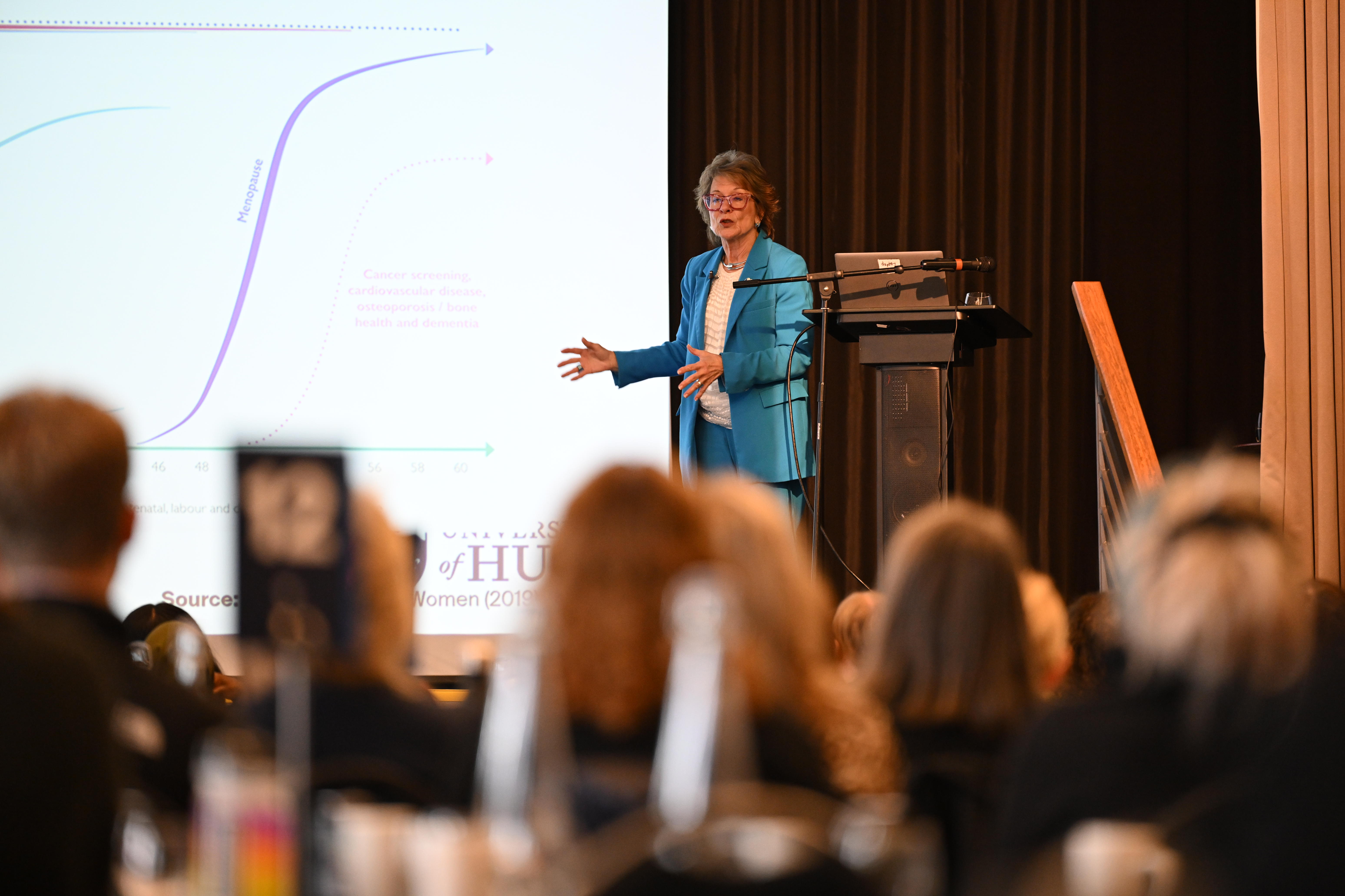 woman in blue suit making a presentation on a stage in front of a slide