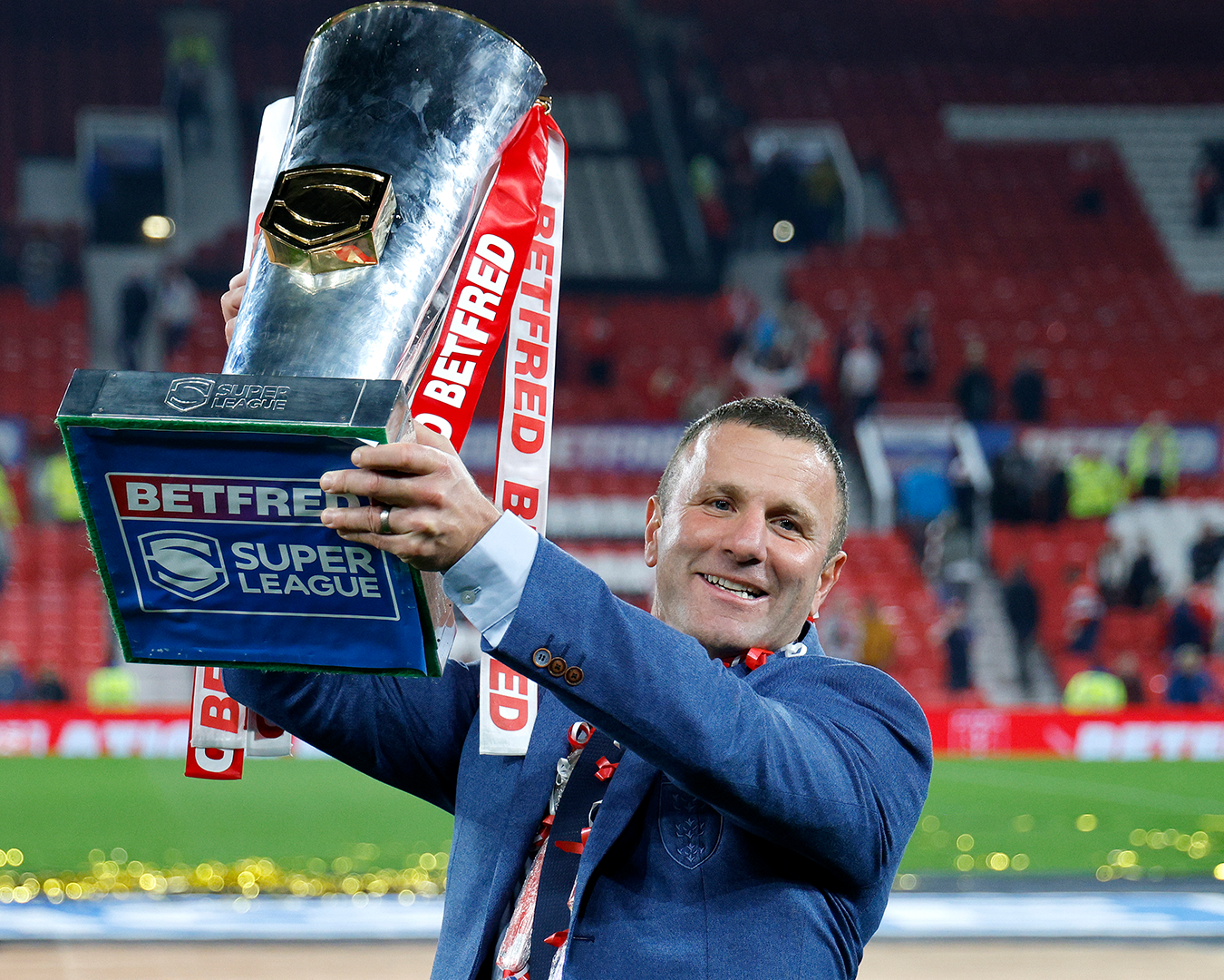 man in blue suit holding trophy aloft
