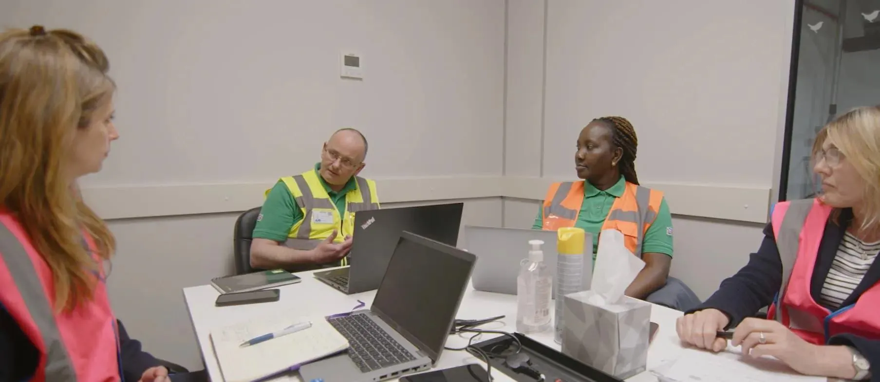 People sat at table with laptops in hi-vis jackets