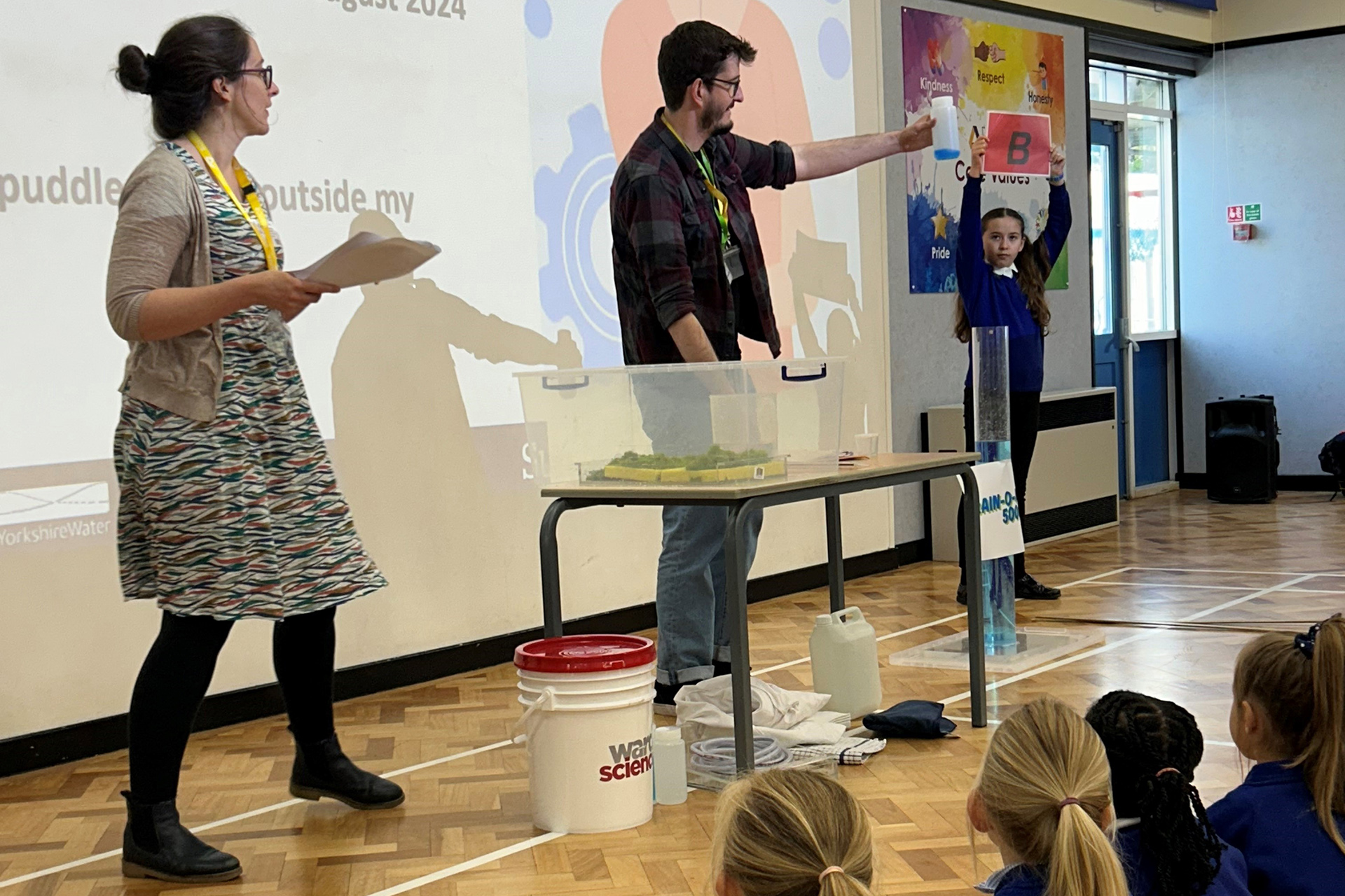 Two researchers lead an assembly for primary school children