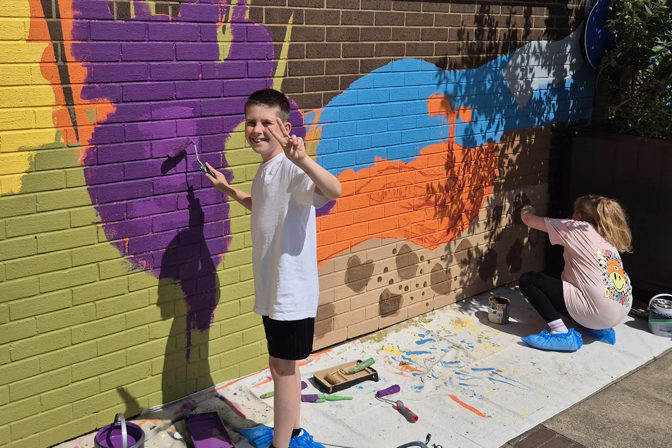 Two schoolchildren paint a colourful mural