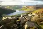 View over a rocky hillside across green hills and a reservoir