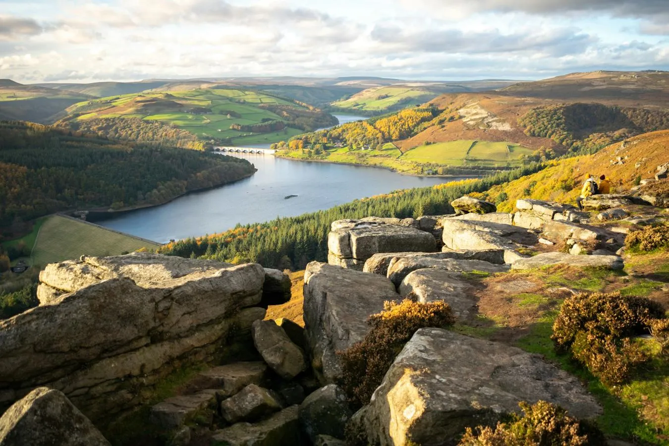 View over a rocky hillside across green hills and a reservoir