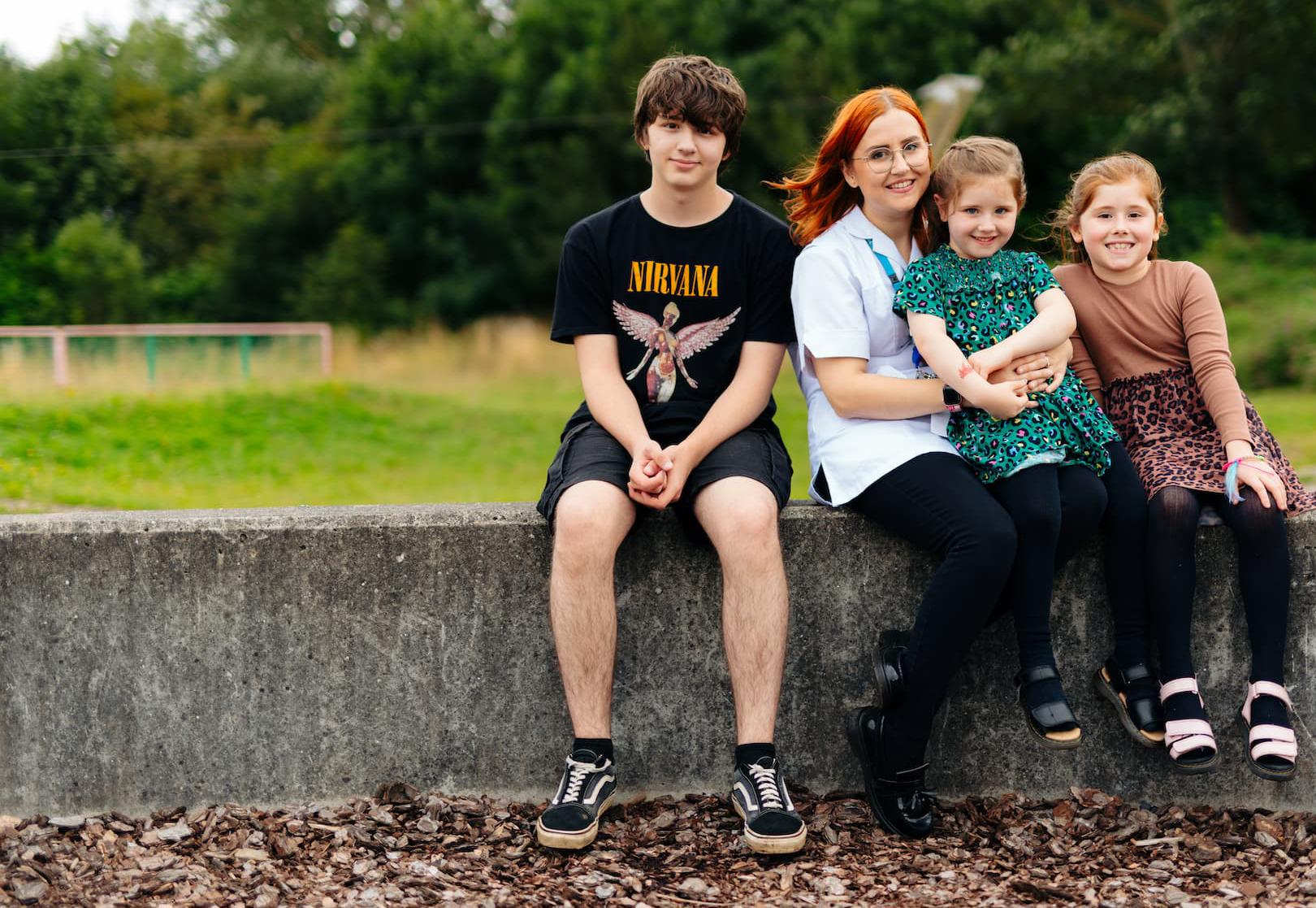 A student nurse and three children sat on a park wall