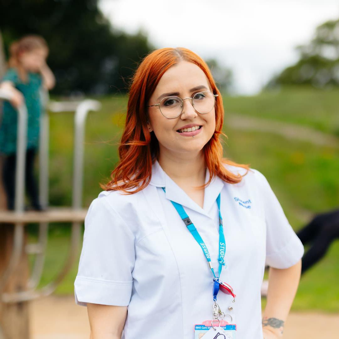 A student nurse with three children playing on equipment in a park