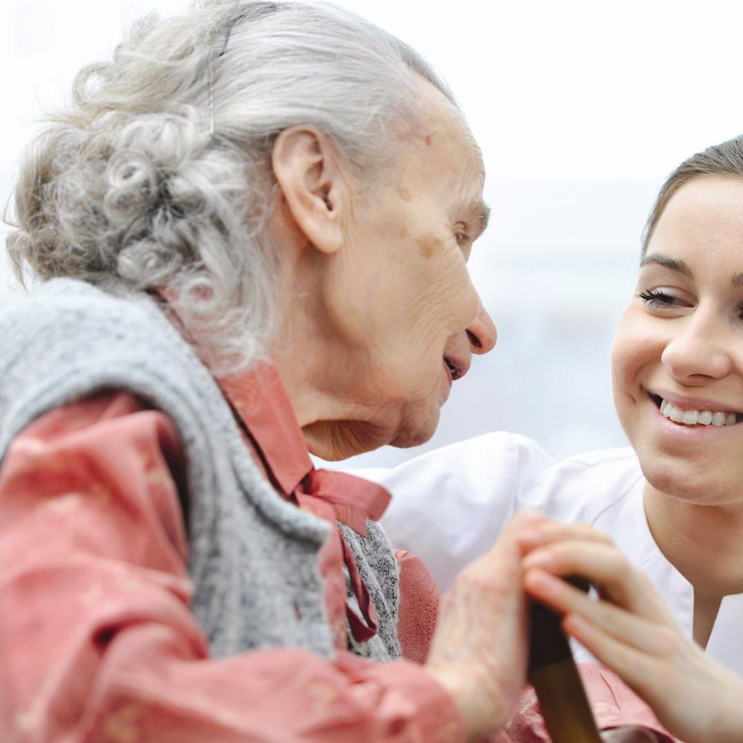 A student nurse smiling at an elderly patient while holding her hand